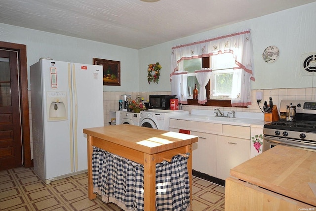 kitchen with backsplash, stainless steel range, sink, white refrigerator with ice dispenser, and washer and dryer