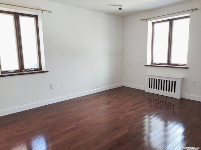 unfurnished room with dark hardwood / wood-style flooring, a wealth of natural light, and radiator heating unit