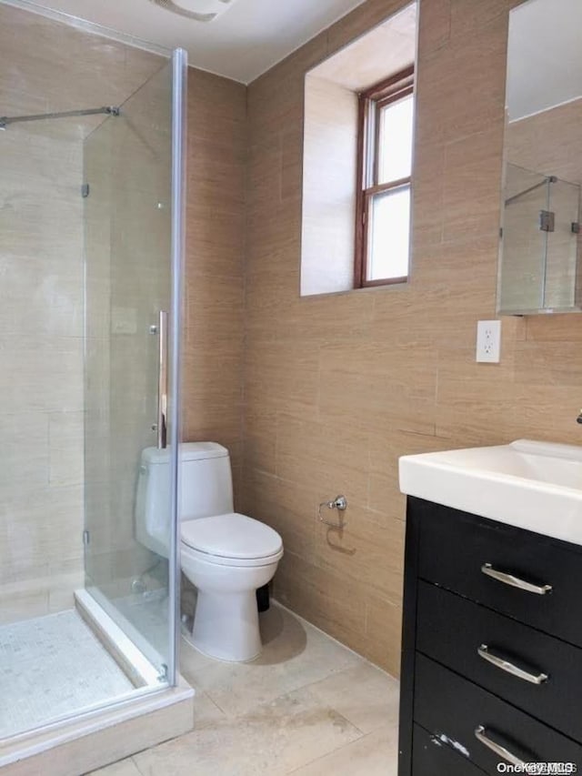 bathroom featuring vanity, tile patterned flooring, toilet, tile walls, and a shower with shower door