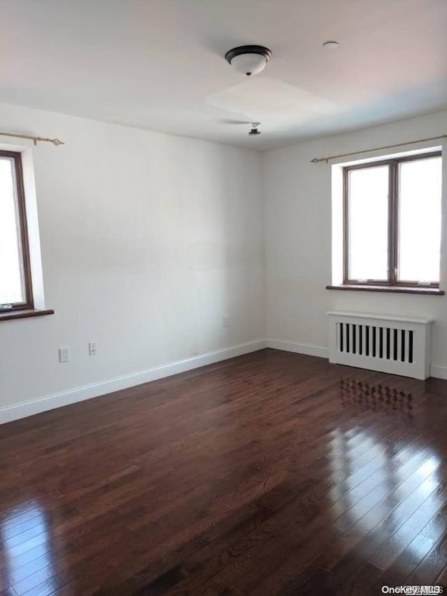 empty room featuring dark hardwood / wood-style flooring, radiator, and a healthy amount of sunlight