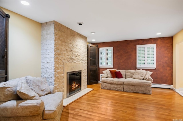 living room featuring light wood-type flooring, a stone fireplace, and baseboard heating