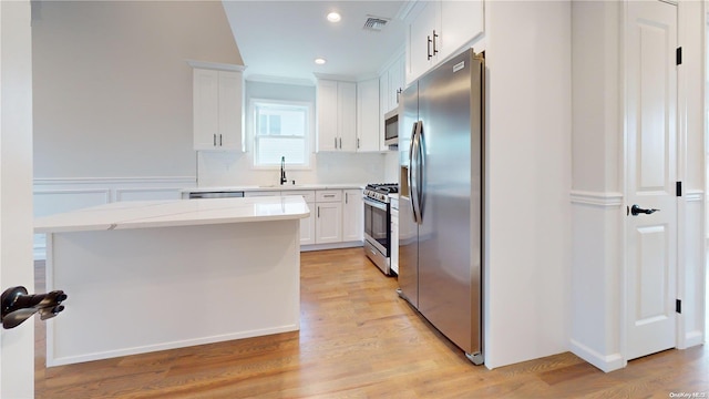 kitchen with light stone countertops, white cabinets, appliances with stainless steel finishes, sink, and light hardwood / wood-style flooring