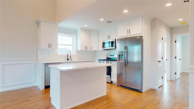 kitchen with appliances with stainless steel finishes, sink, white cabinets, light hardwood / wood-style flooring, and a center island