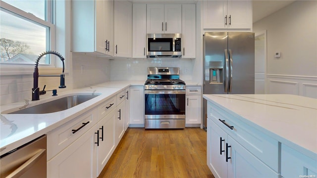 kitchen with white cabinetry, light hardwood / wood-style floors, stainless steel appliances, light stone countertops, and sink