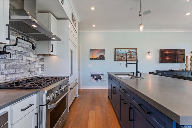 kitchen with wall chimney exhaust hood, stainless steel range, sink, blue cabinetry, and white cabinetry