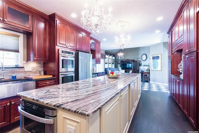 kitchen with an inviting chandelier, hanging light fixtures, dark hardwood / wood-style floors, appliances with stainless steel finishes, and tasteful backsplash