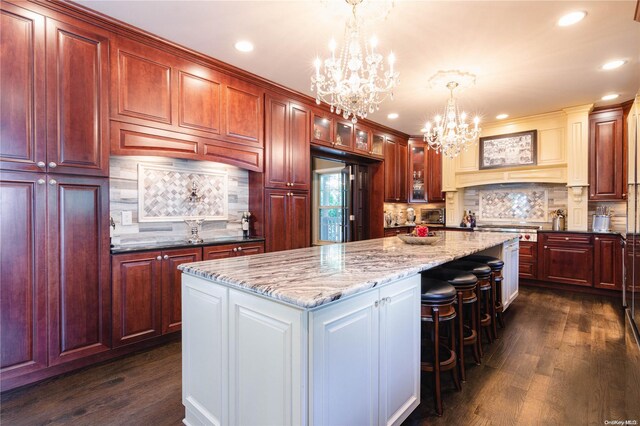 kitchen featuring premium range hood, dark wood-type flooring, decorative light fixtures, a notable chandelier, and a kitchen island