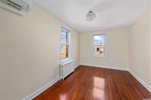 spare room featuring radiator heating unit, dark wood-type flooring, and an AC wall unit