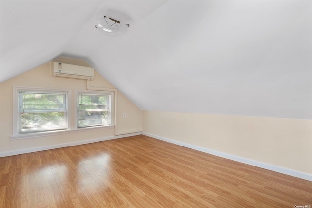 additional living space with a wall unit AC, light hardwood / wood-style floors, and vaulted ceiling