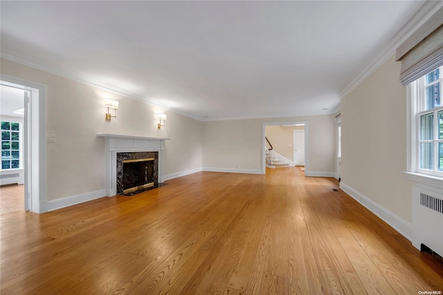 unfurnished living room featuring a premium fireplace, radiator heating unit, crown molding, and light hardwood / wood-style flooring