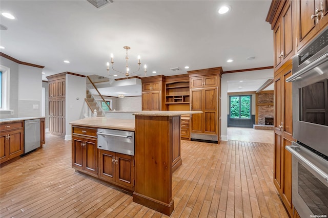 kitchen with a fireplace, an inviting chandelier, stainless steel appliances, and light hardwood / wood-style flooring