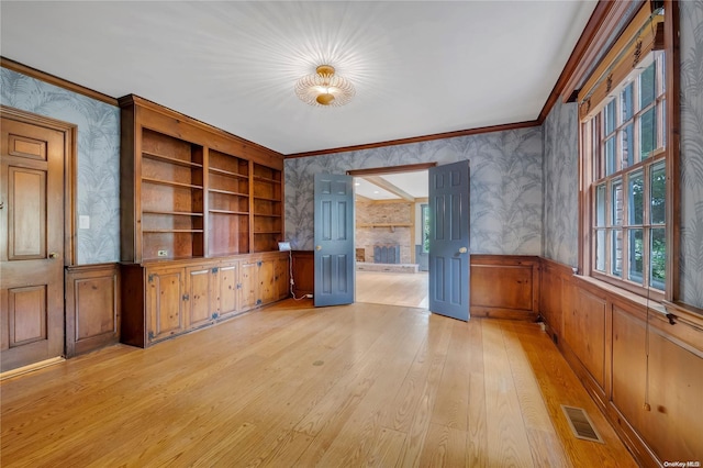 unfurnished living room with built in shelves, light hardwood / wood-style floors, and crown molding