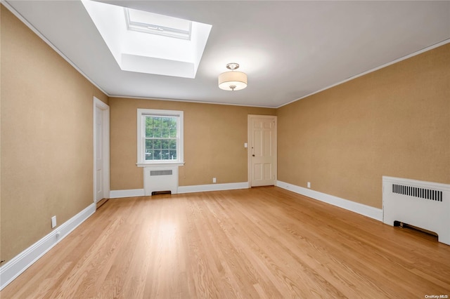 unfurnished living room featuring a skylight, radiator heating unit, ornamental molding, and light wood-type flooring