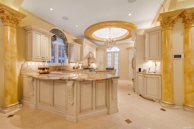 kitchen featuring cream cabinetry, decorative light fixtures, ornate columns, and sink