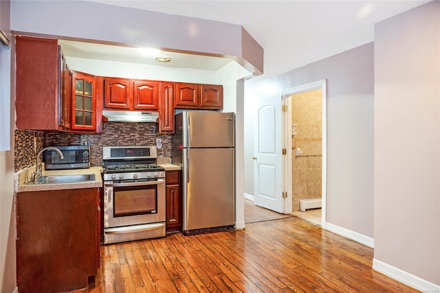 kitchen featuring baseboard heating, stainless steel appliances, decorative backsplash, sink, and hardwood / wood-style flooring