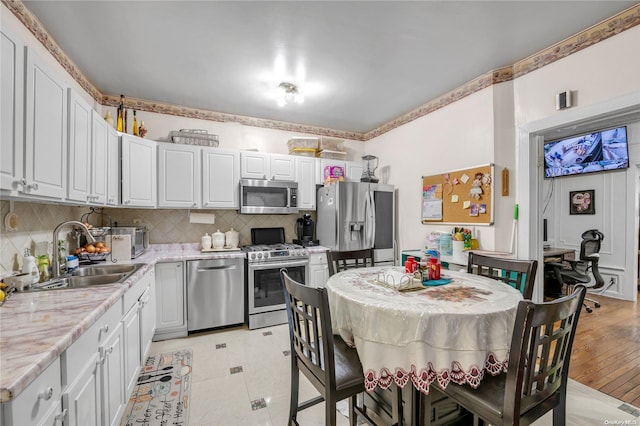 kitchen with white cabinetry, sink, stainless steel appliances, light hardwood / wood-style floors, and decorative backsplash