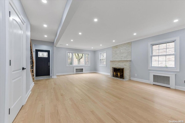 unfurnished living room with a healthy amount of sunlight, light hardwood / wood-style floors, a fireplace, and radiator