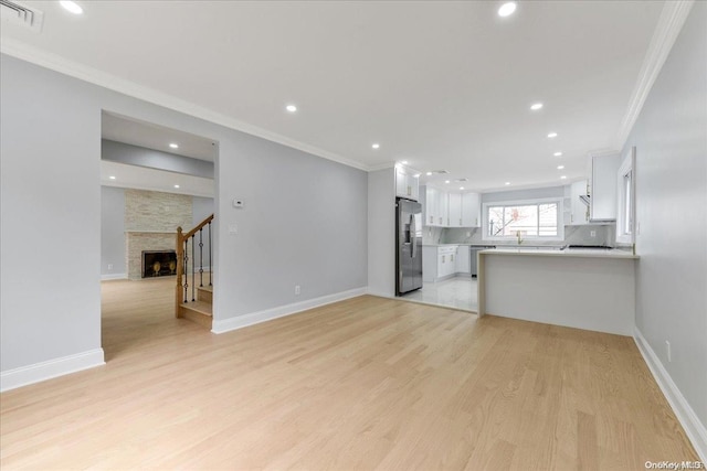 unfurnished living room featuring light hardwood / wood-style floors, a stone fireplace, and ornamental molding