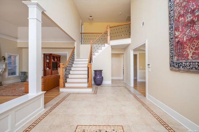 foyer entrance with light tile patterned flooring, ornamental molding, a high ceiling, and decorative columns