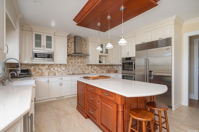 kitchen with a center island, wall chimney exhaust hood, sink, backsplash, and built in appliances