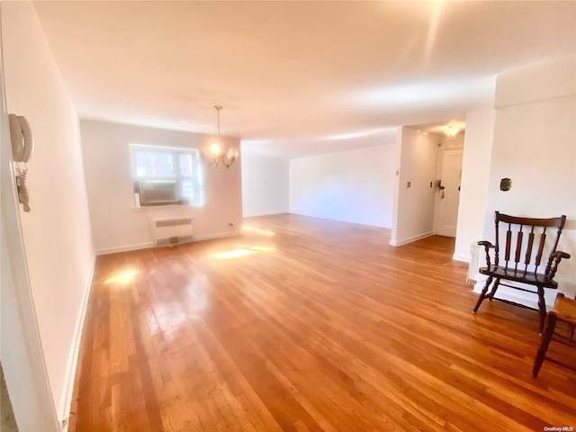 empty room with light hardwood / wood-style floors, an inviting chandelier, and radiator