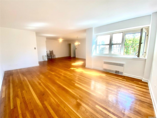 unfurnished living room with radiator heating unit, an inviting chandelier, and hardwood / wood-style floors