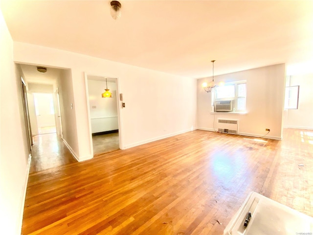 unfurnished living room featuring hardwood / wood-style flooring, an inviting chandelier, radiator, and cooling unit