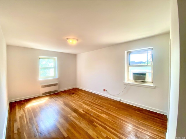 empty room with cooling unit, hardwood / wood-style flooring, radiator, and a healthy amount of sunlight