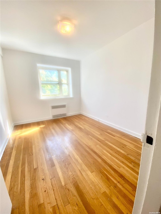 empty room featuring radiator heating unit and hardwood / wood-style flooring