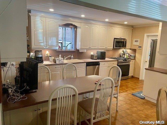 kitchen featuring stainless steel appliances, white cabinetry, crown molding, and sink