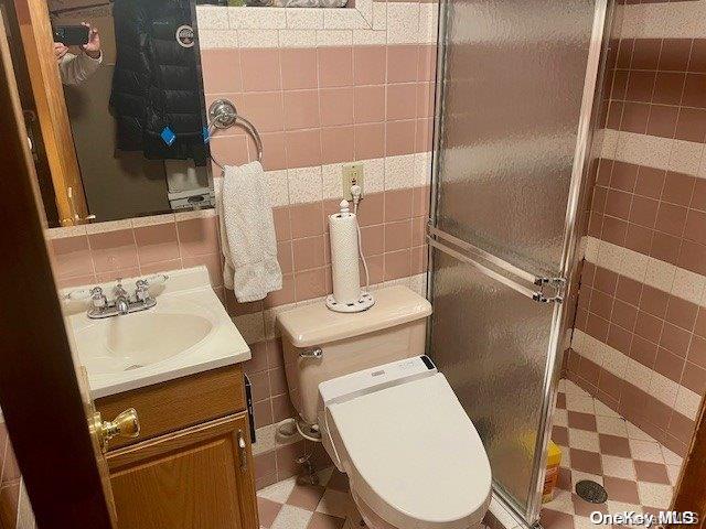 bathroom featuring a shower with door, vanity, tile walls, and toilet