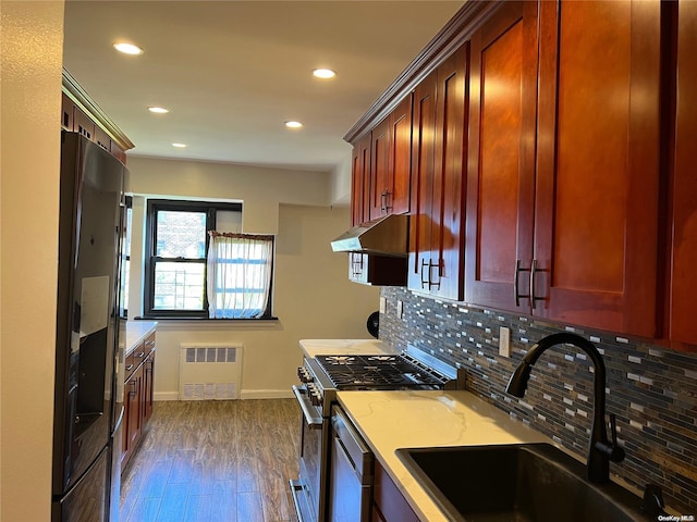 kitchen featuring sink, dark hardwood / wood-style floors, appliances with stainless steel finishes, tasteful backsplash, and radiator heating unit