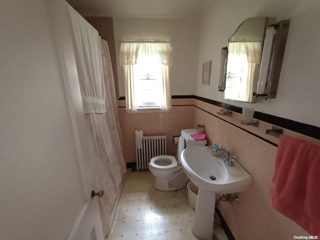 bathroom featuring tile walls, sink, radiator heating unit, and toilet