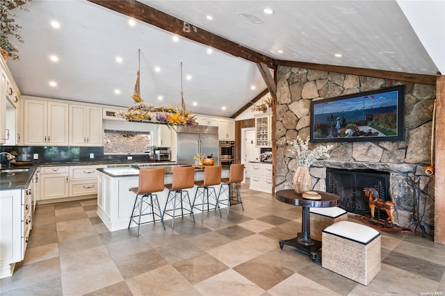 kitchen with a kitchen bar, a center island, stainless steel appliances, a fireplace, and vaulted ceiling with beams