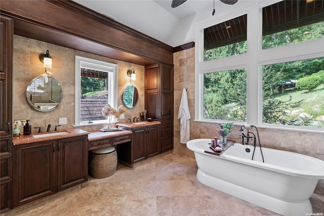 bathroom with tile patterned floors, a washtub, vanity, vaulted ceiling, and tile walls