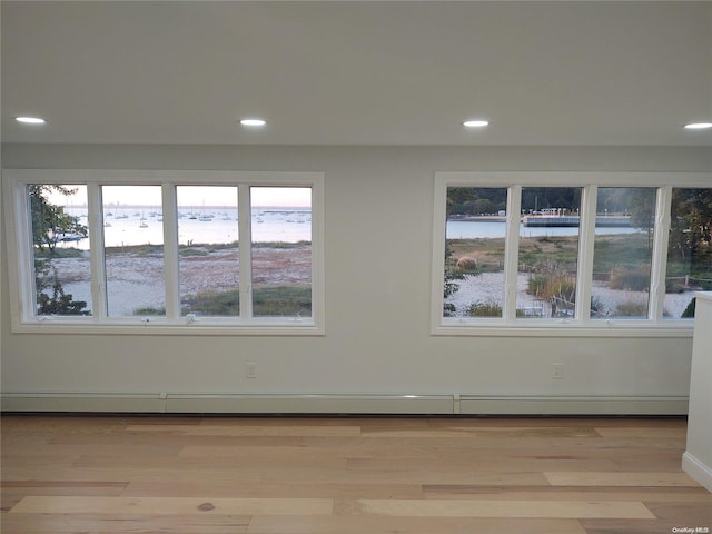 empty room featuring a water view, a wealth of natural light, light hardwood / wood-style floors, and a baseboard radiator