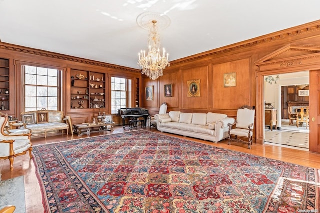 living room with wood walls, light wood-type flooring, built in features, ornamental molding, and a notable chandelier