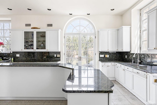 kitchen with sink, a kitchen island, backsplash, dark stone countertops, and white cabinets