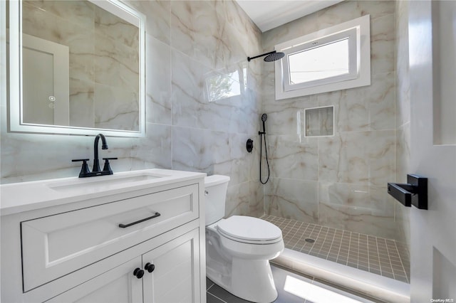 bathroom with vanity, toilet, tiled shower, and tile walls