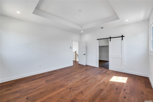 unfurnished bedroom featuring a barn door, dark hardwood / wood-style floors, a raised ceiling, and a closet