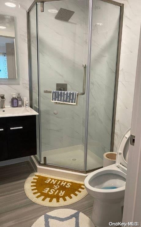 bathroom featuring vanity, tile walls, tasteful backsplash, an enclosed shower, and wood-type flooring