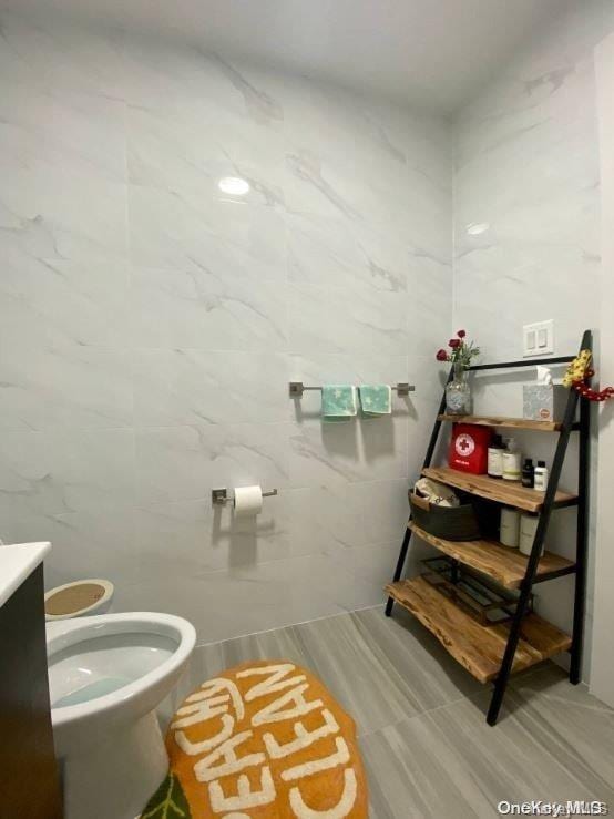 bathroom featuring vanity, toilet, and tile walls