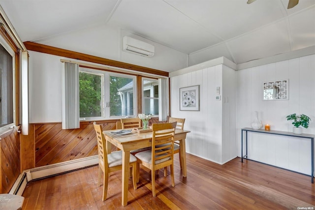 dining room with wood-type flooring, vaulted ceiling, a wall unit AC, and wood walls