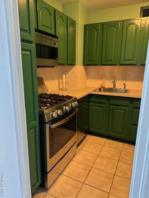 kitchen featuring sink, light tile patterned floors, appliances with stainless steel finishes, backsplash, and green cabinetry