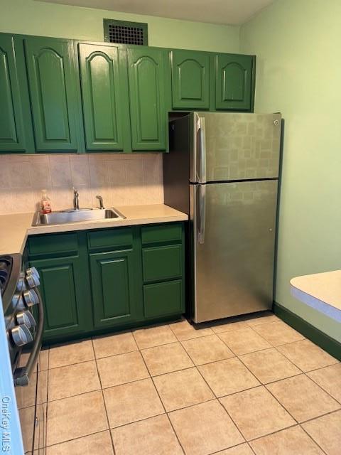 kitchen featuring sink, light tile patterned floors, appliances with stainless steel finishes, backsplash, and green cabinetry