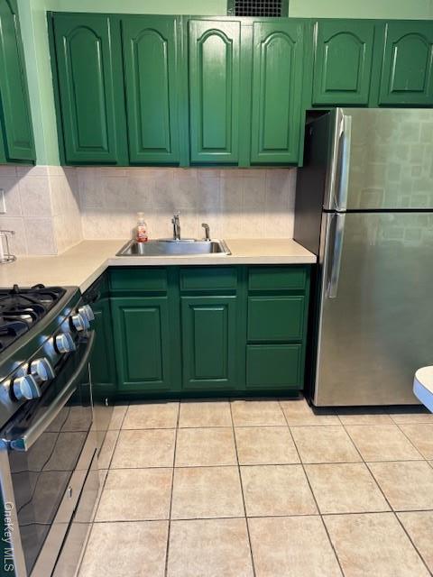 kitchen featuring sink, green cabinetry, light tile patterned floors, appliances with stainless steel finishes, and decorative backsplash