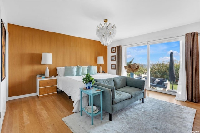 bedroom with an inviting chandelier, access to exterior, wooden walls, and light hardwood / wood-style flooring