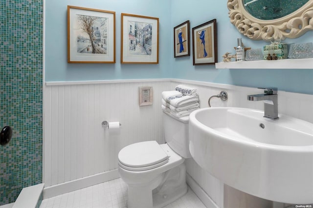 bathroom with wood walls, a shower, sink, toilet, and tile patterned floors