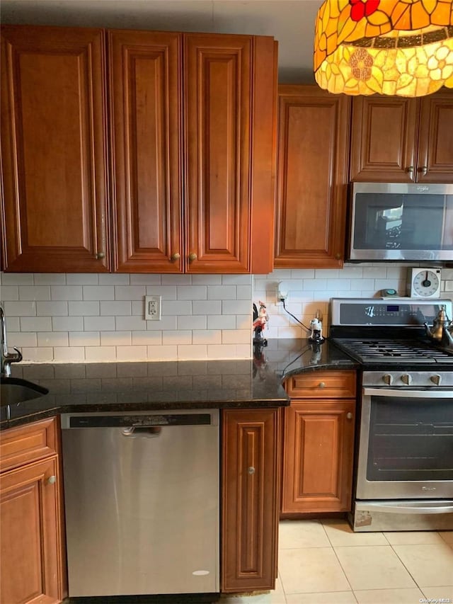 kitchen with sink, backsplash, dark stone counters, light tile patterned flooring, and appliances with stainless steel finishes