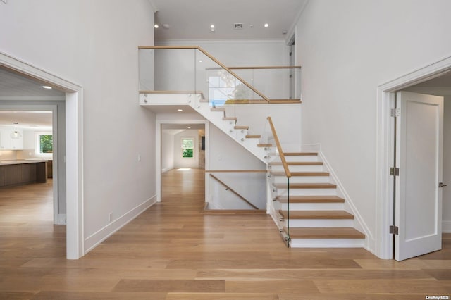 staircase featuring hardwood / wood-style floors, ornamental molding, and a towering ceiling